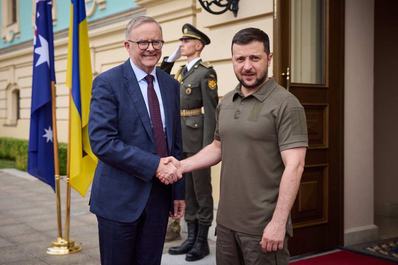 Anthony Albanese (left) and Volodmyr Zelenskyy shake hands while standing outside a building