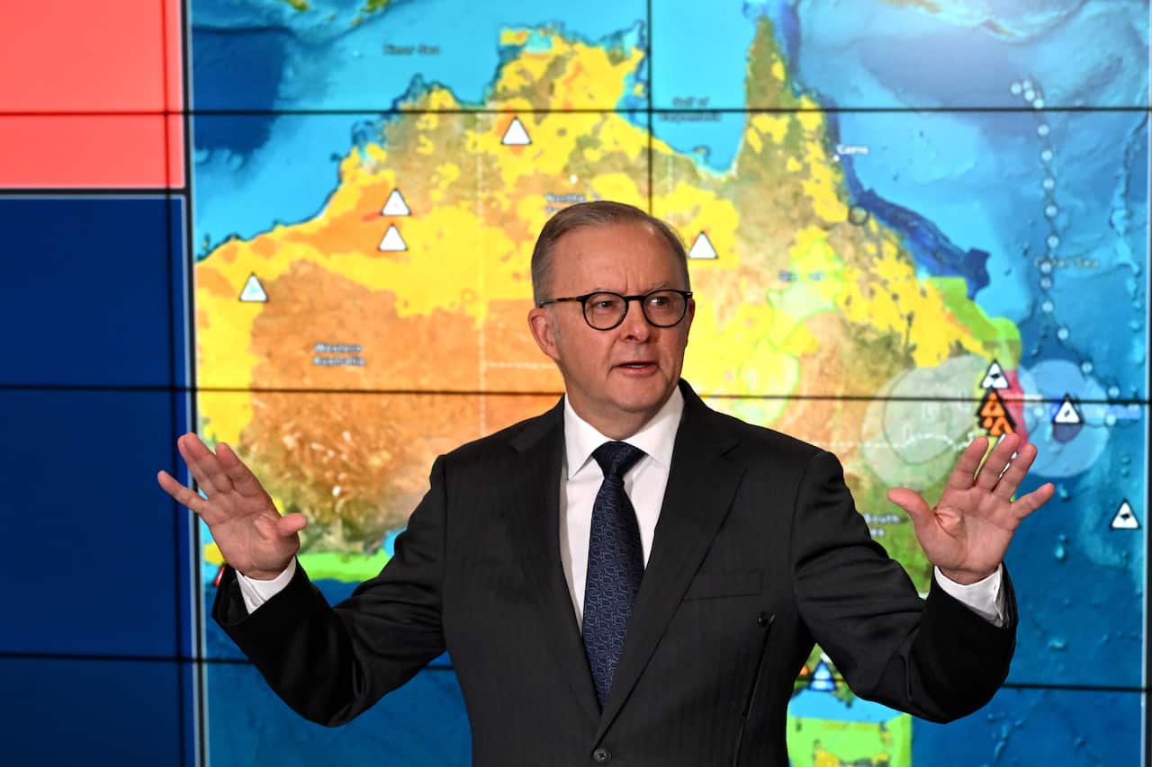 A man in a suit speaking in front of a weather map of Australia