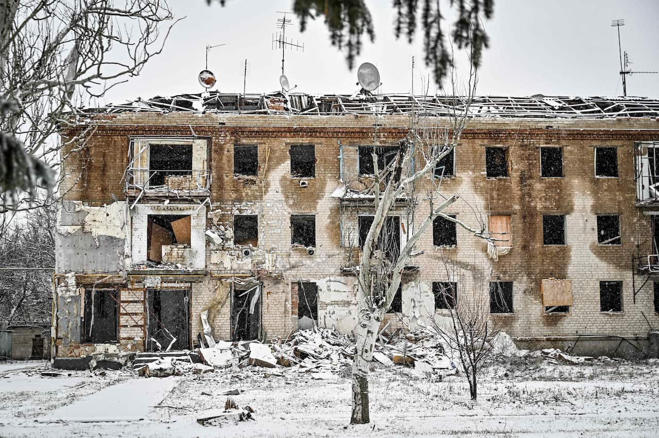 A building damaged by shelling, with dried trees in the foreground.
