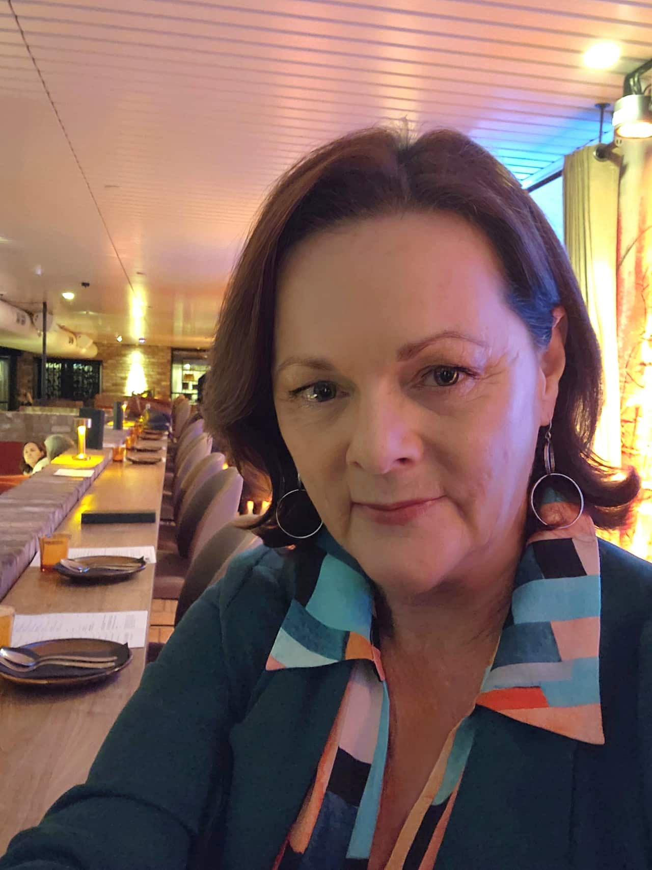 A selfie of a woman in a restaurant with a neutral expression on her face.