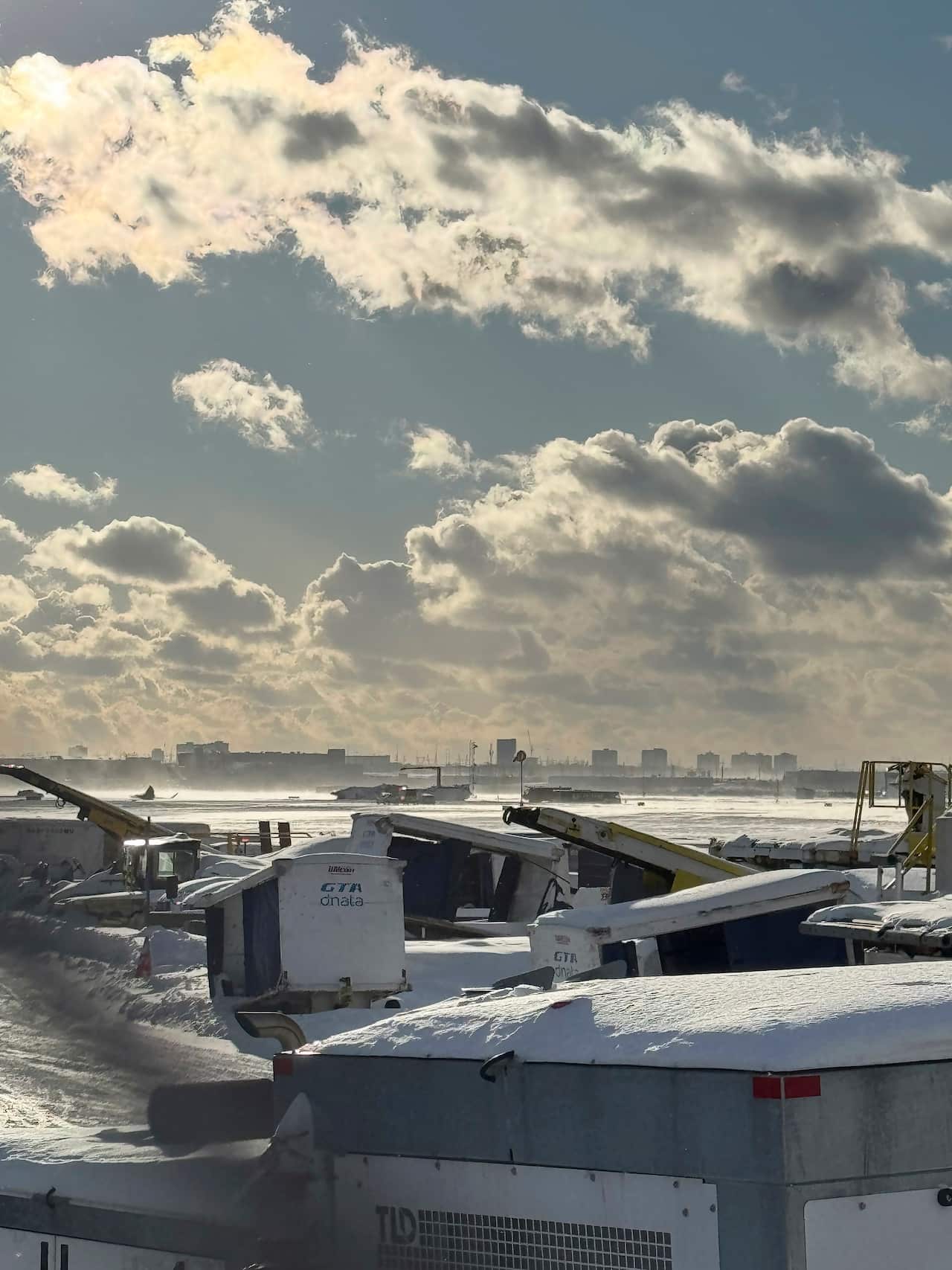 Cranes and air stairs sit on a snow-covered tarmac, with an upside-down plane visible in the distance.