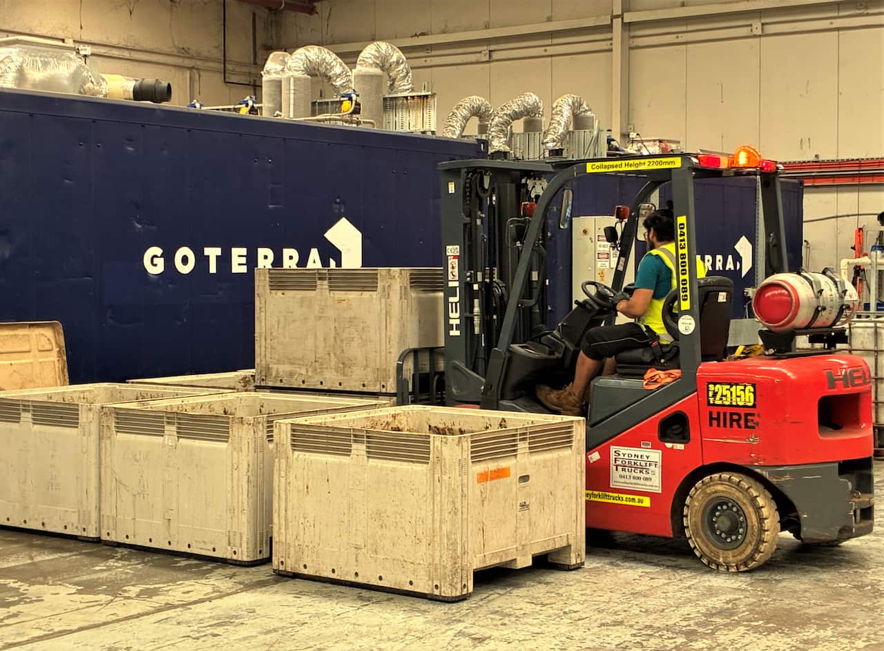 A bobcat moves white crates around a factory floor. 
