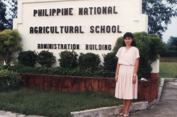 A young woman stands outside a sign for a school.