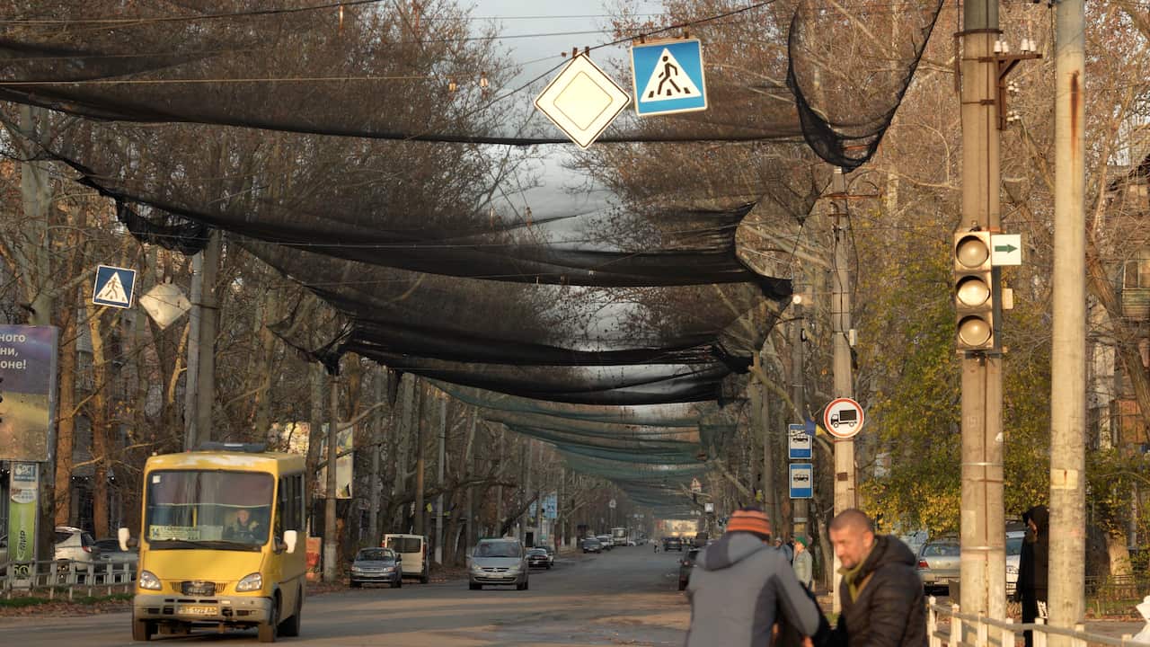 A city street is covered by black netting, with cars driving beneath it.