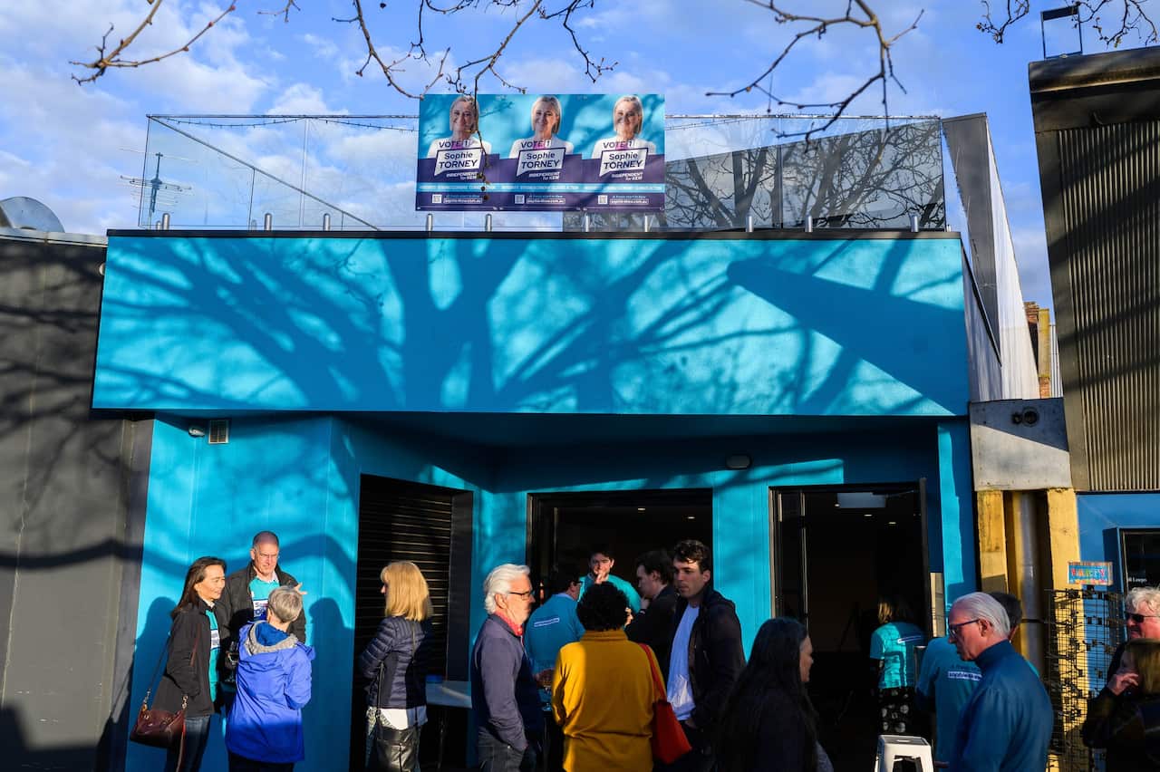 People mill about in front of a teal building. 