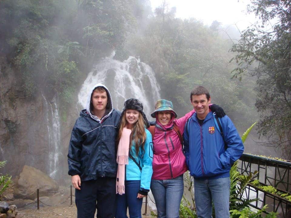 A mum and dad with their son and daughter standing and smiling in front of a waterfall.