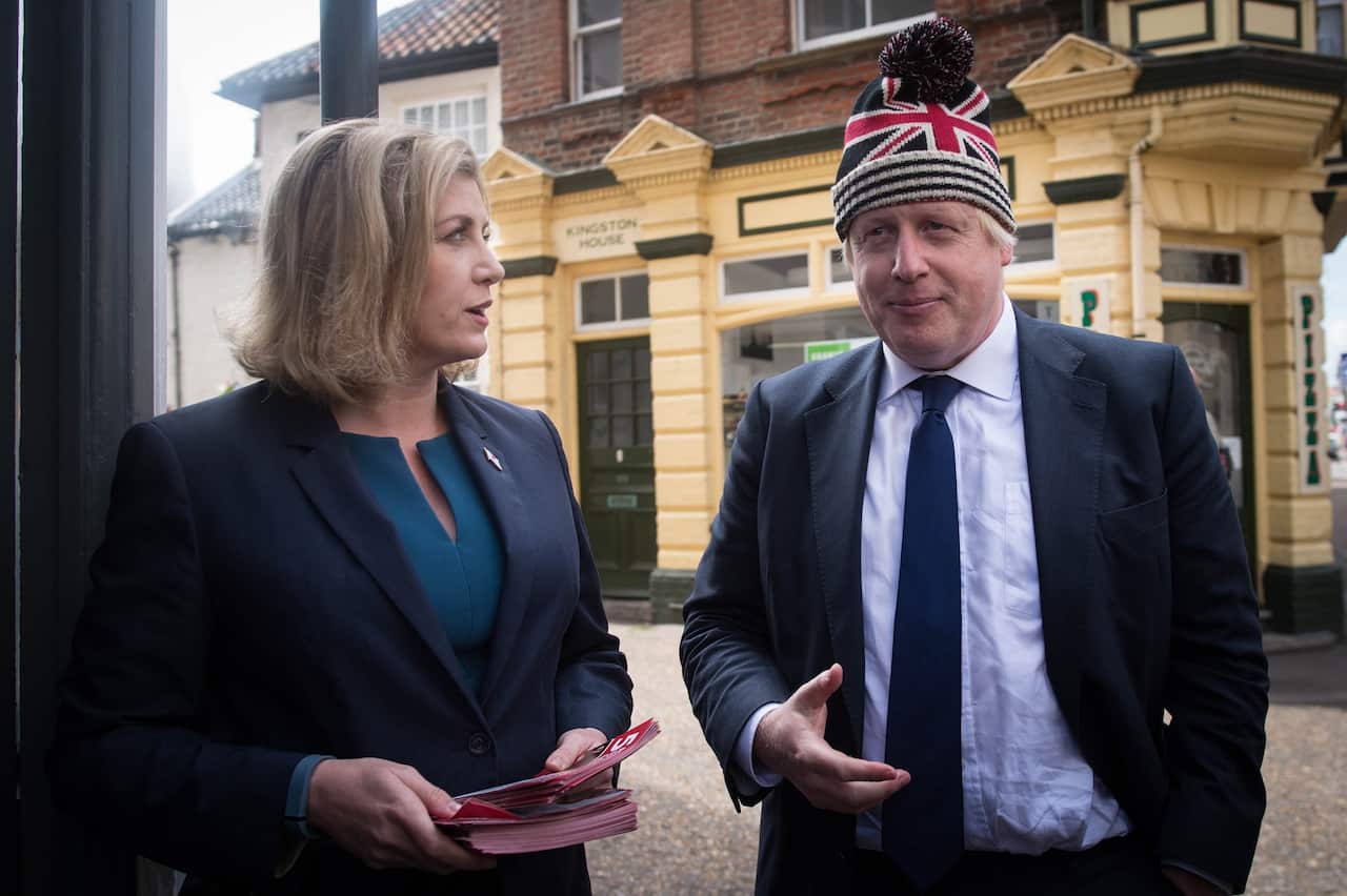 Penny Mordaunt looks to her left at Boris Johnson who is wearing a beanie with the UK flag on it. 