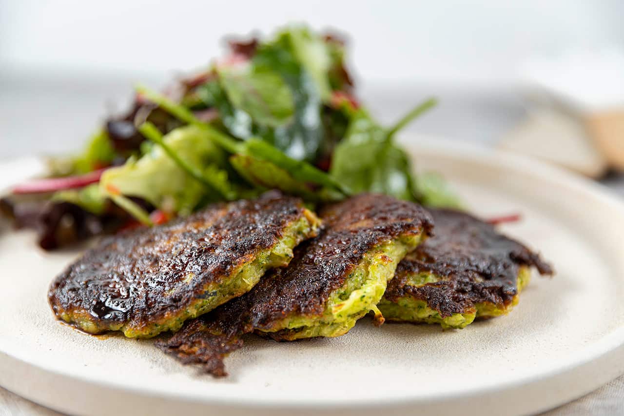 Three green fritters sit on a plate, with a pile of salad leaves. 