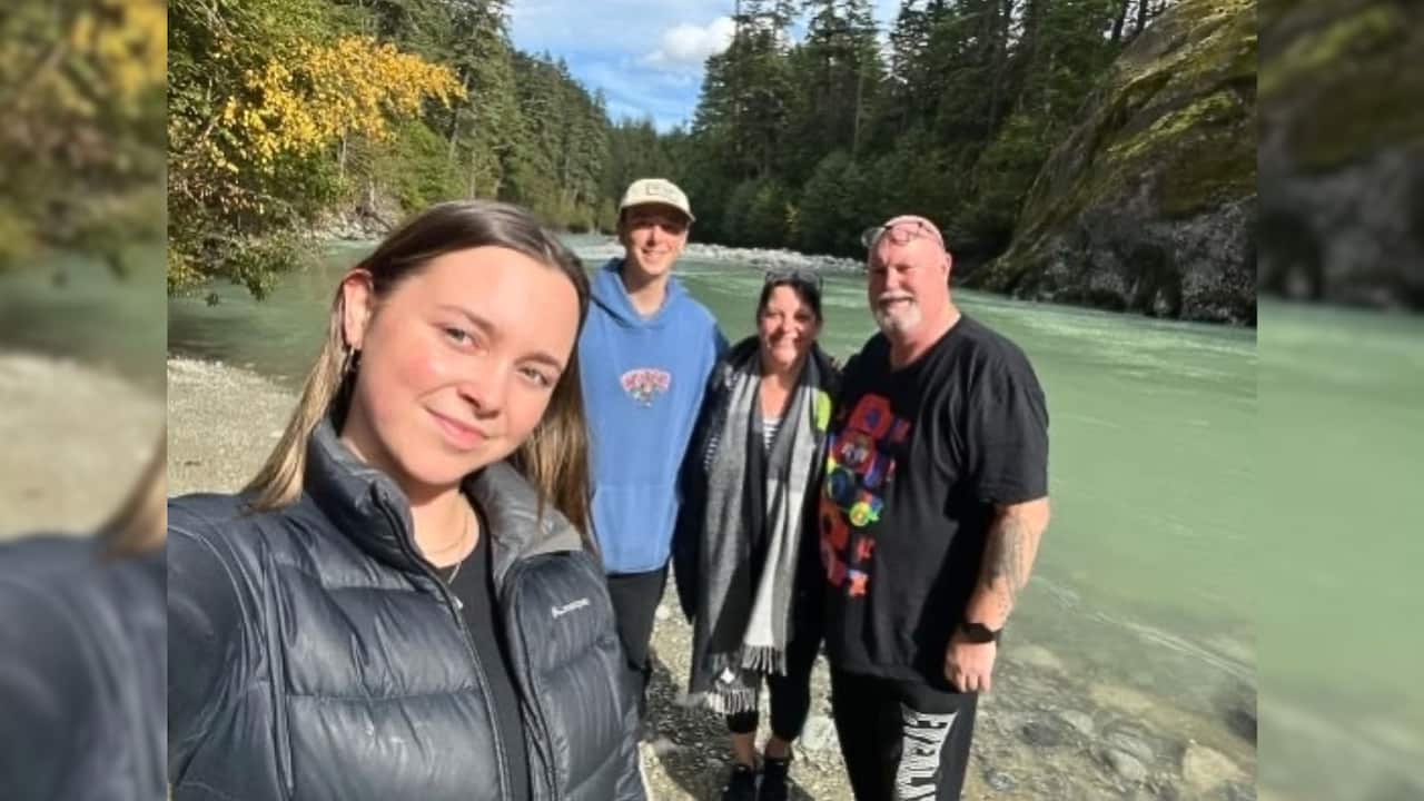 a family of a teenage girl, teenage son, middle aged woman and man take a selfie in front of a light green river