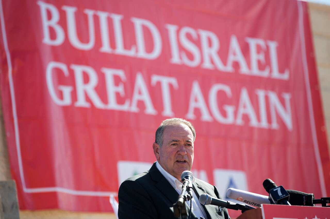 A man speaking into microphones at a podium. A giant red flag behind him reads: 'Build Israel great again'.