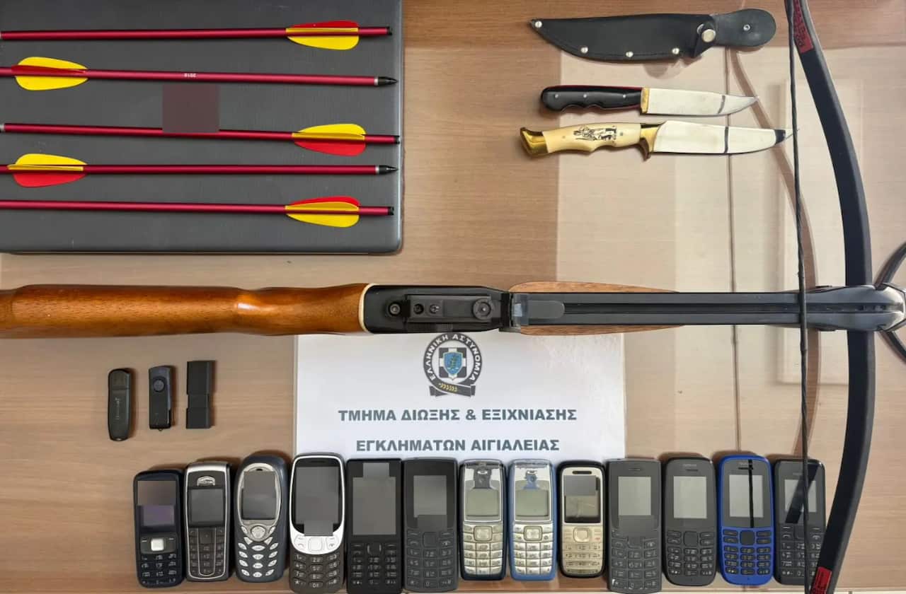 A bow and arrow, 13 mobile phones, USB sticks, knives and a white sheet with Greek writing laid out on a table