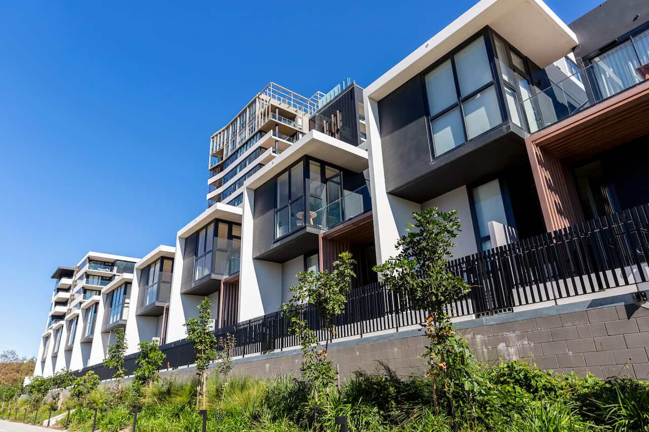 A row of modern townhouses with green plants and trees underneath them.