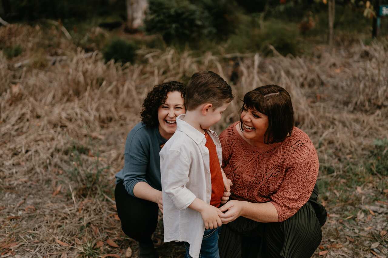 Two women laugh as they play with their son outside.