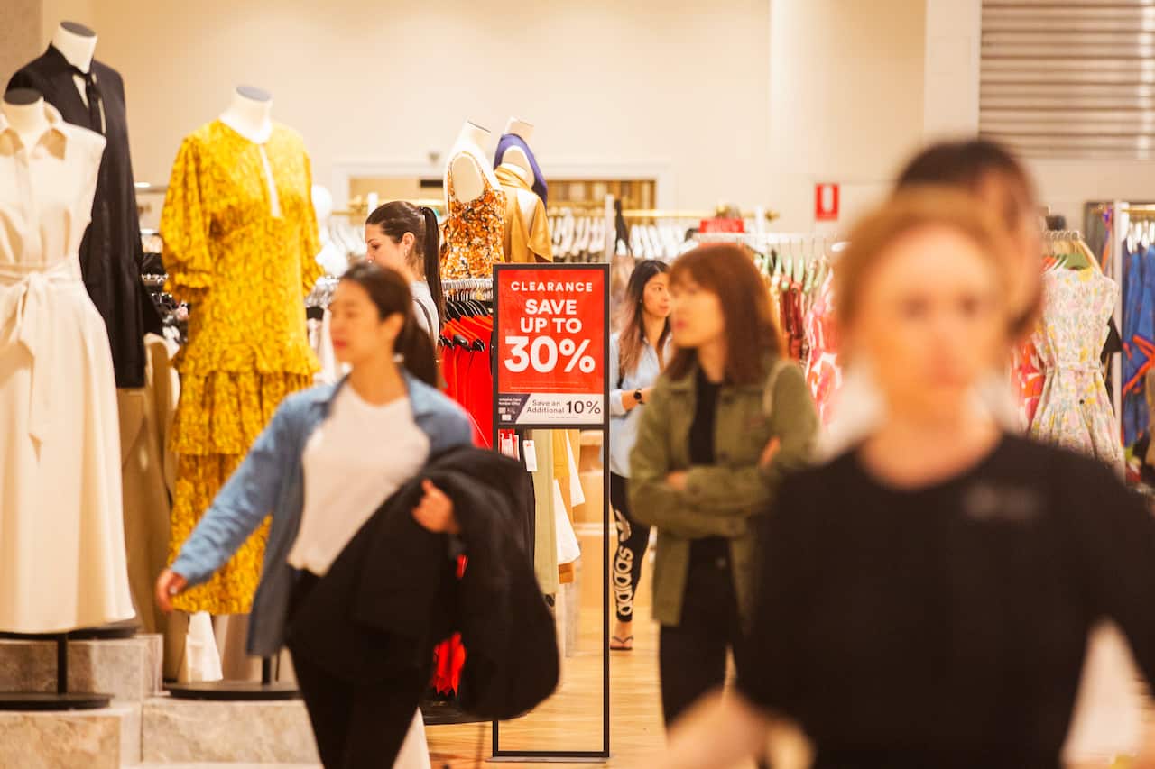 Blurred figures move through a shop, with a sign advertising a sale.