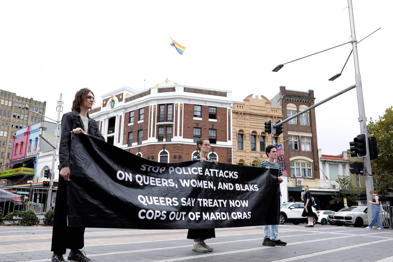 Three people hold up a black banner with white writing
