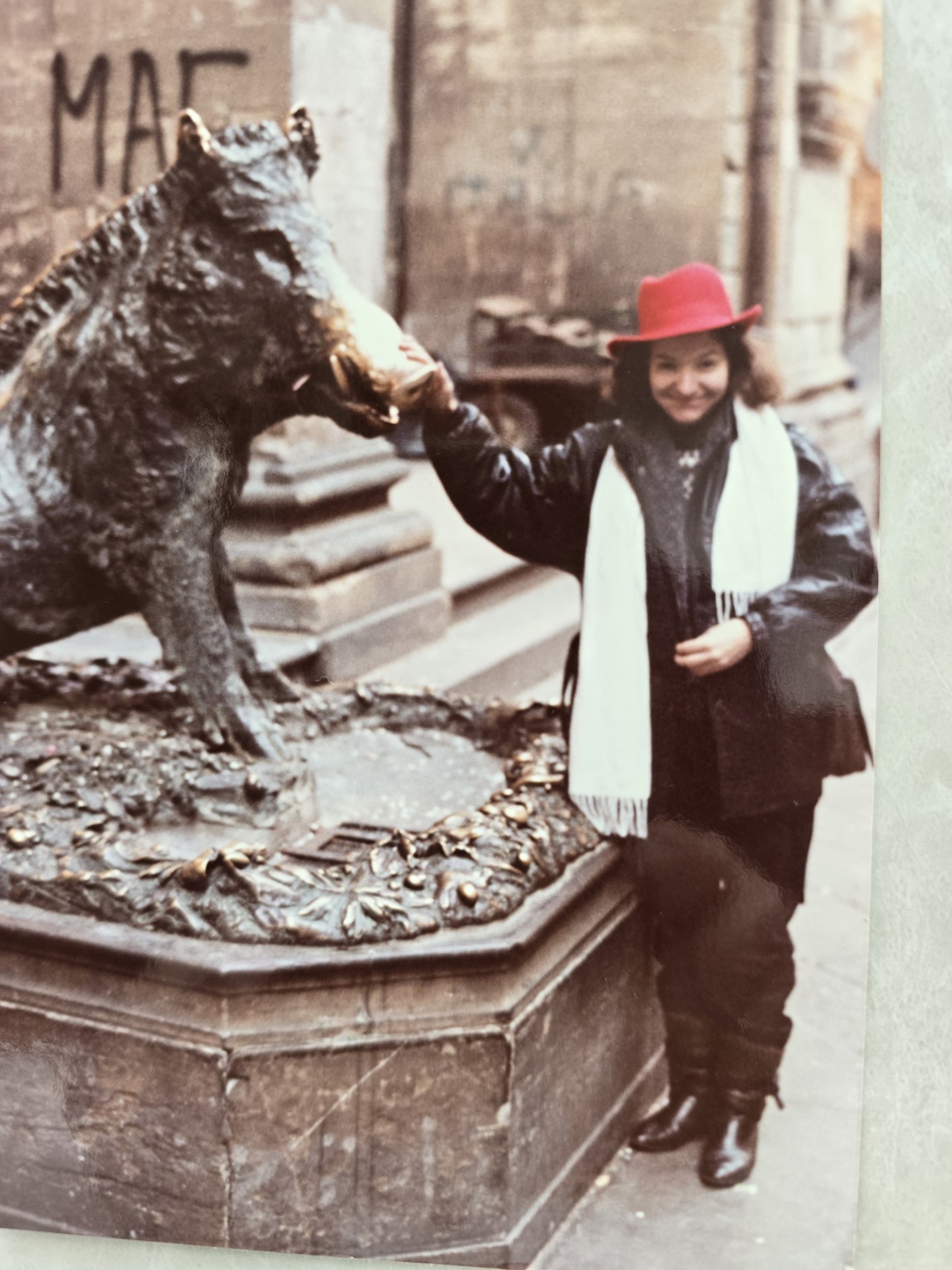 A woman in a red hat and white scarf stands beside a horse statue, touching its head.
