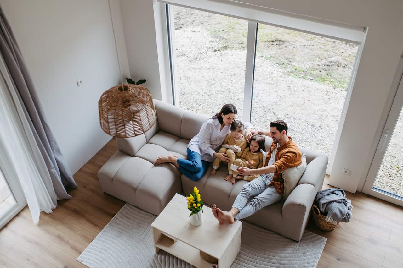 Parents and two children sit on a sofa in a living room while taking a selfie.
