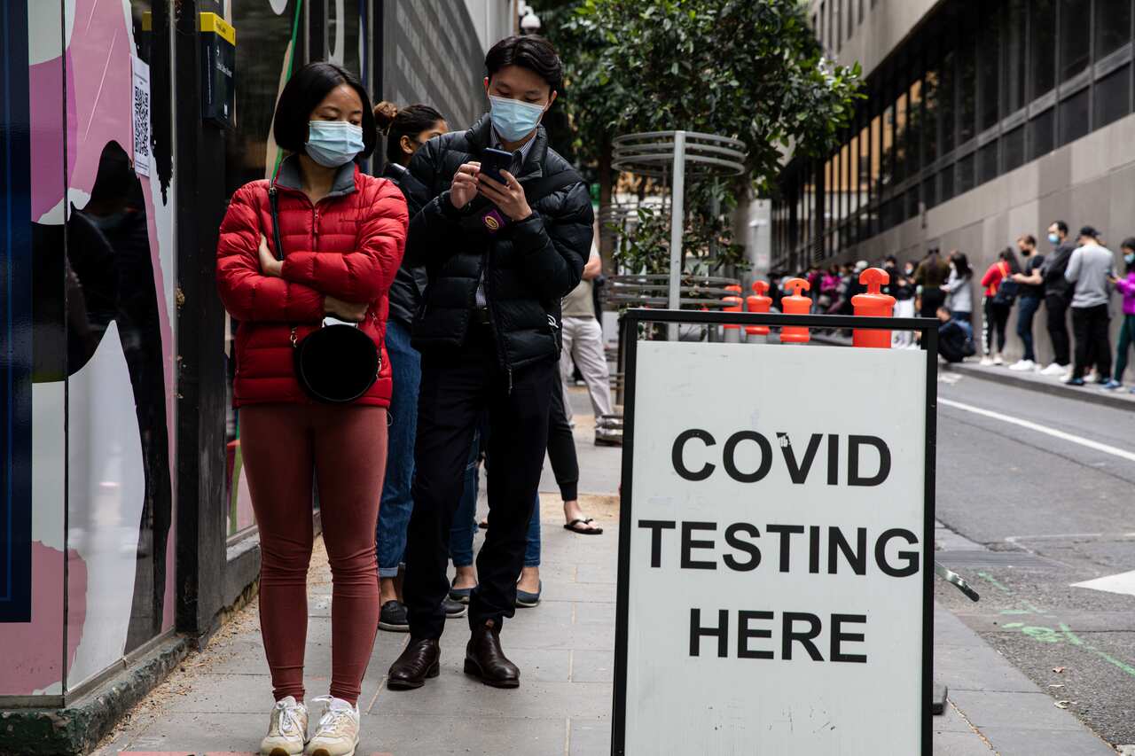 People wearing face masks line up in a street while waiting for COVID testing