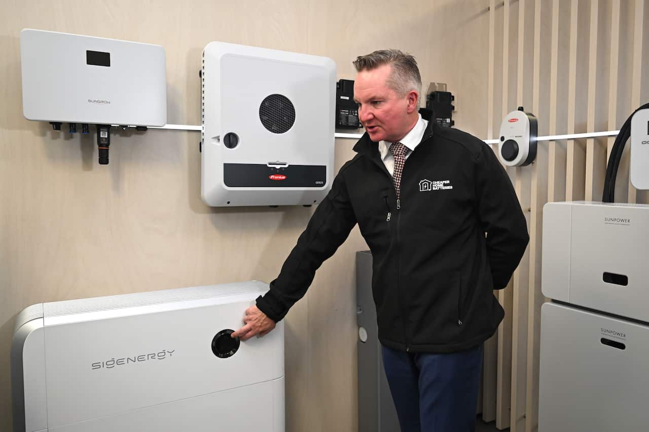 A man in a black jumper stands in a room filled with solar home battery systems.