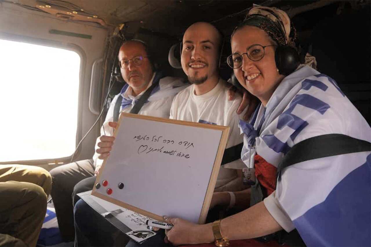 Two men and a woman sitting inside a helicopter, holding a whiteboard with writing on it.