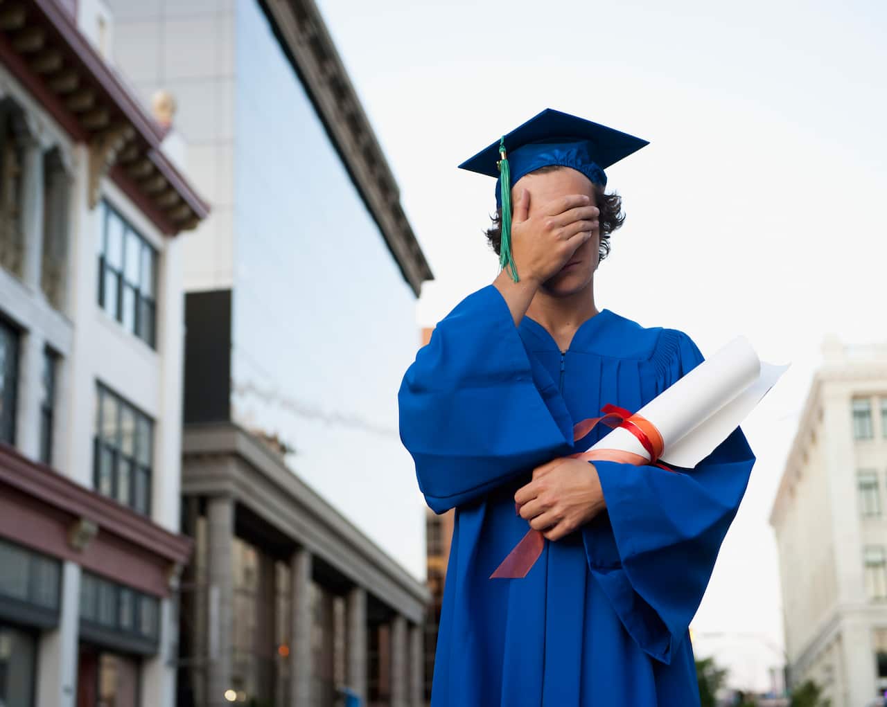 A Graduate In Cap And Gown Holds His Hand Over His Eyes