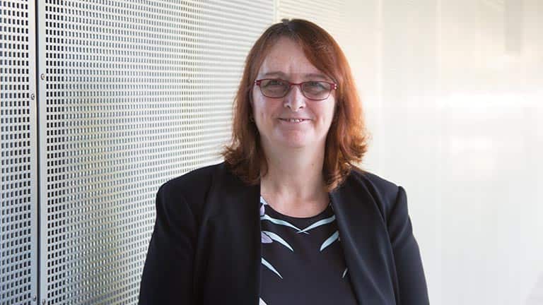 A red-haired woman wearing glasses smiles at the camera.