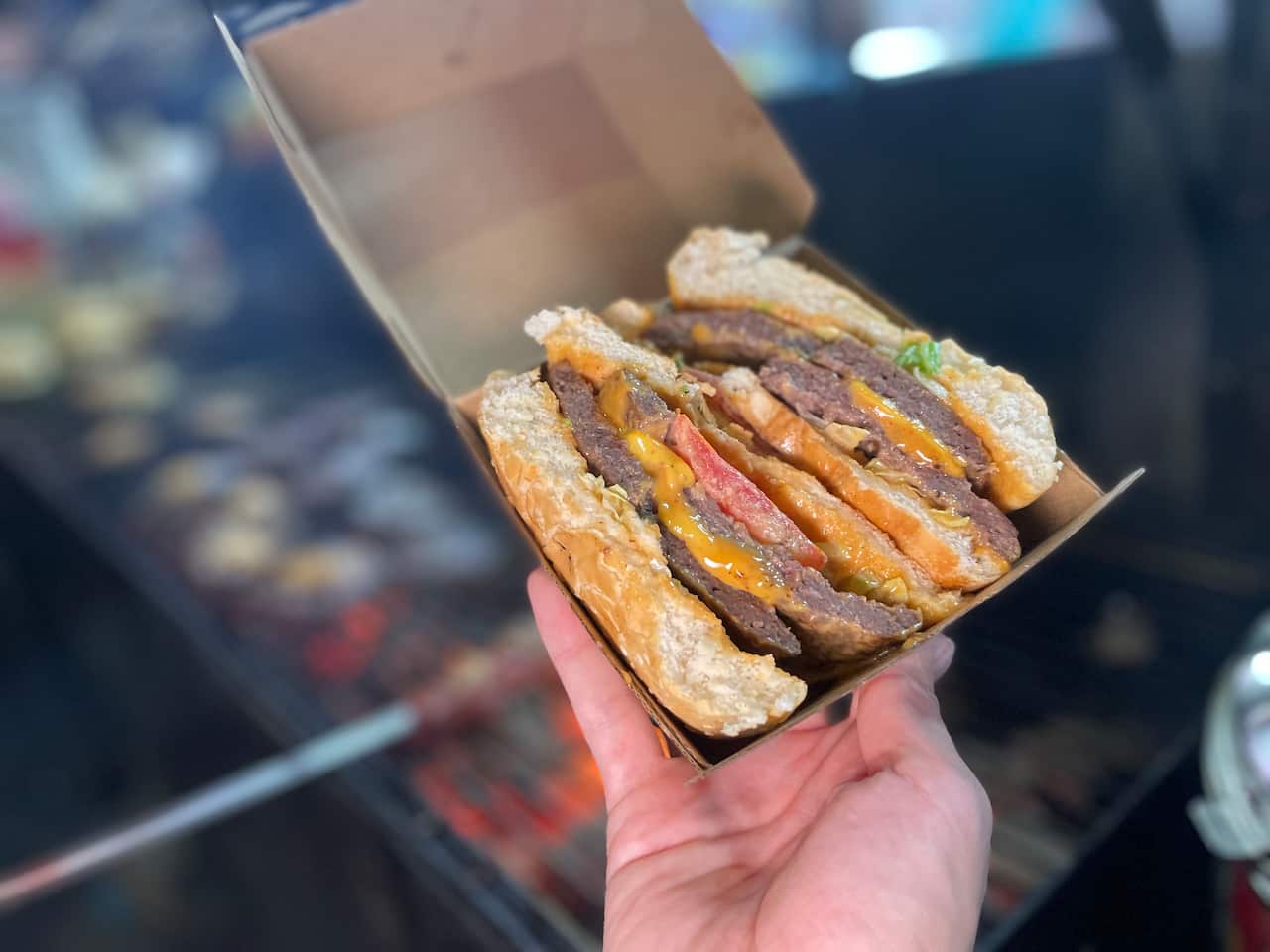 Burger cut in half in a box in front of a barbecue grill. 