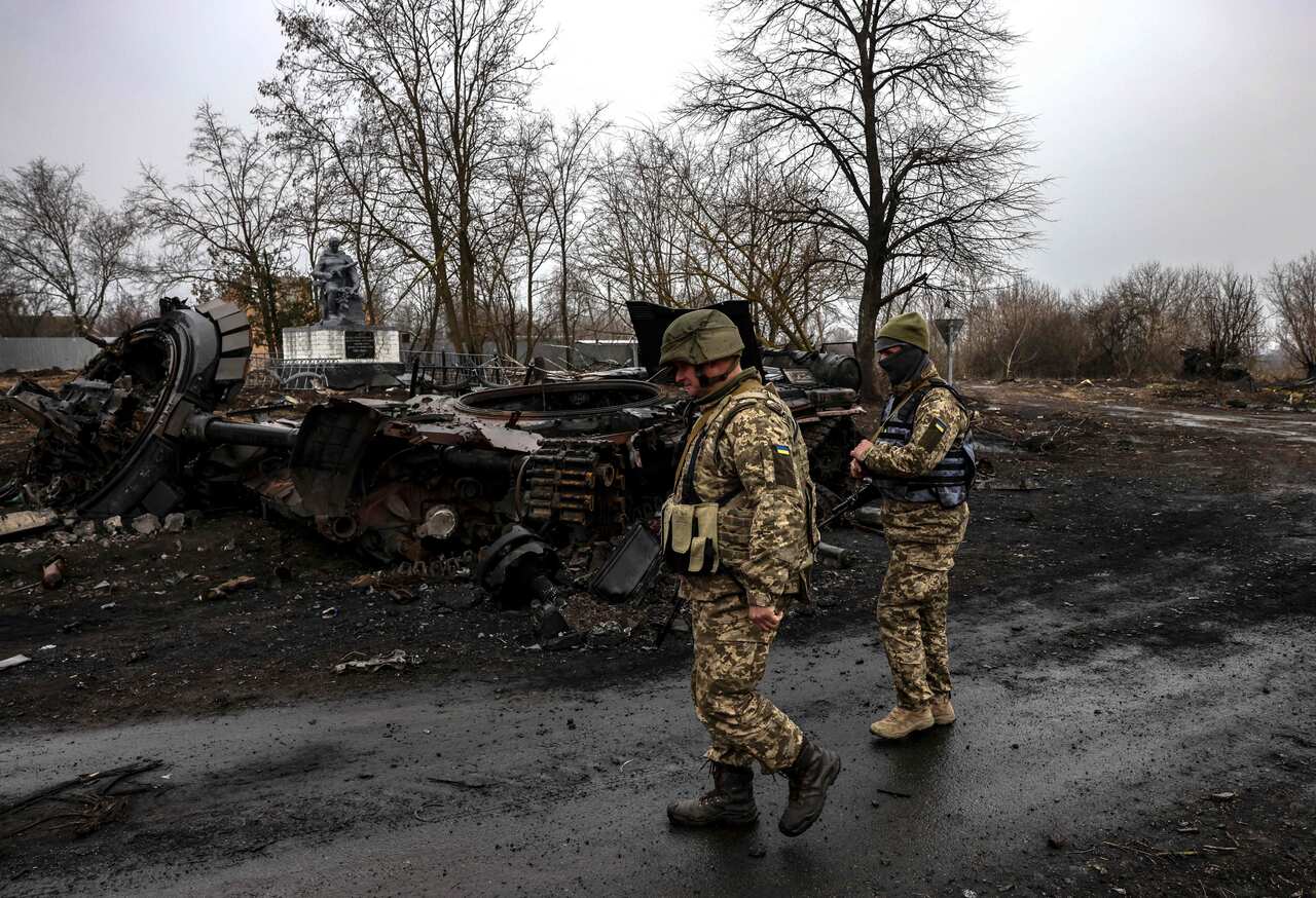 Two Ukrainian soldiers walking next to a destroyed Russian tank.