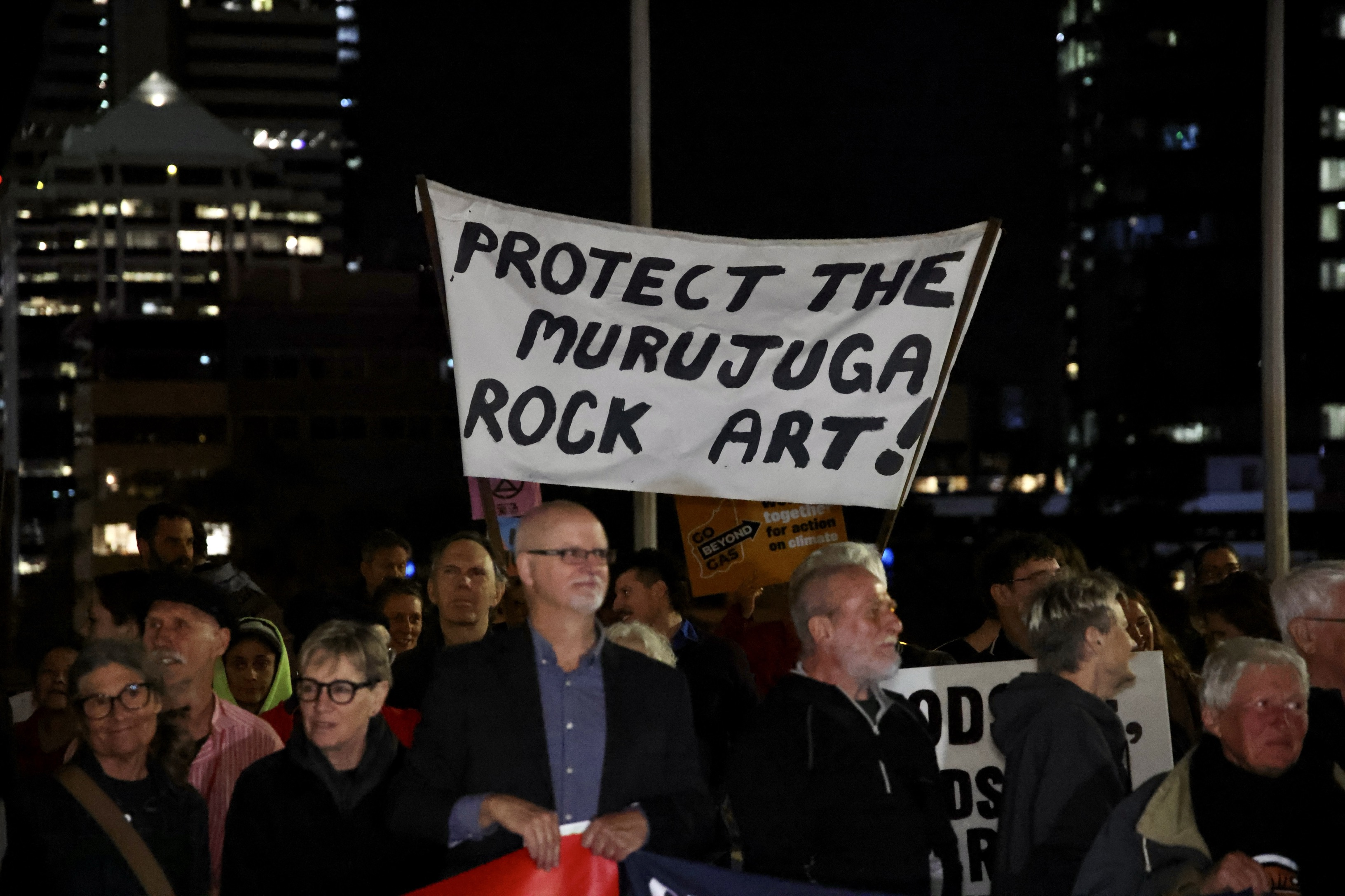 A person holding a sign that reads, "Protect the Murujuga rock art," stands among a crowd of protesters. 