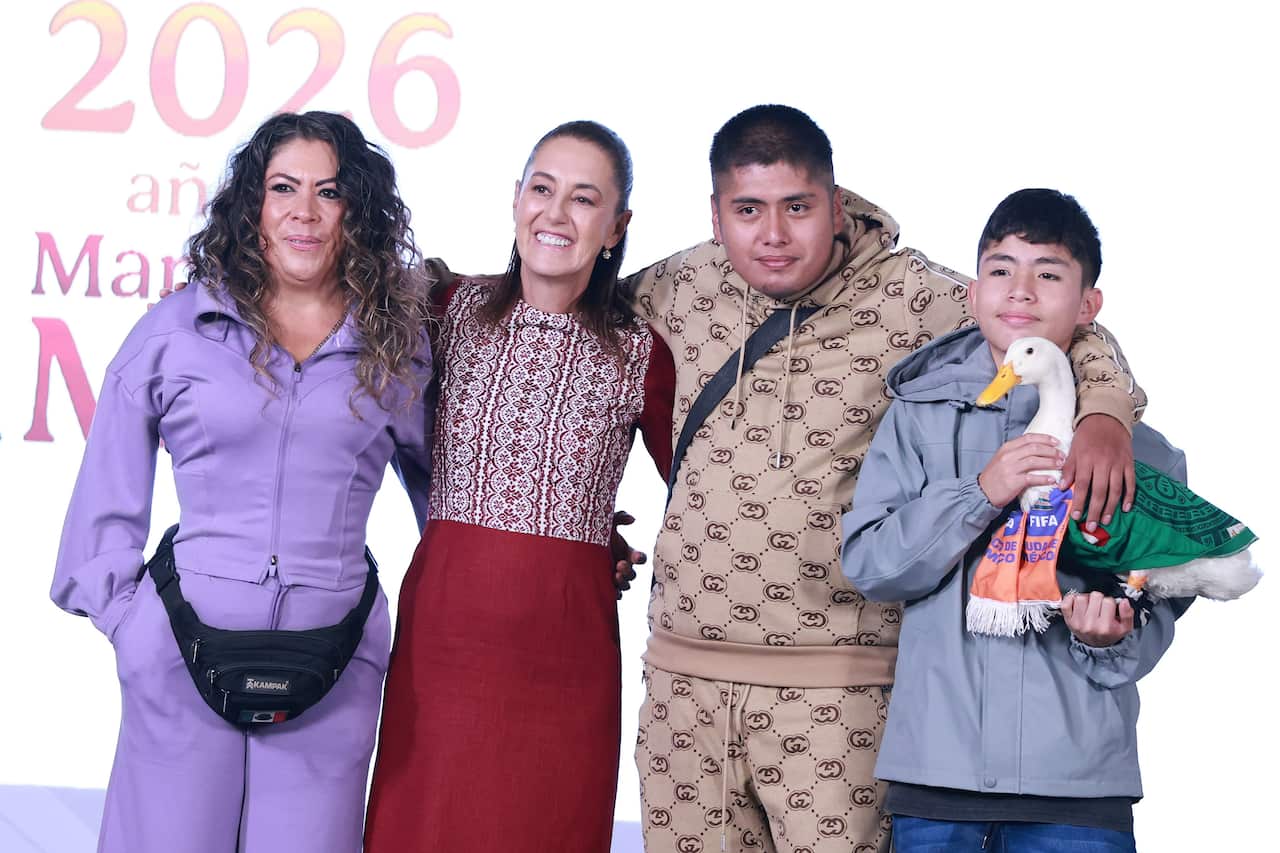 Two women and two boys posing for a photograph on a stage. One of the boys is holding a pet duck dressed in a Mexican football jersey.