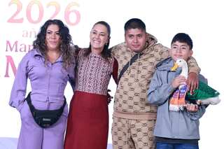 Two women and two boys posing for a photograph on a stage. One of the boys is holding a pet duck dressed in a Mexican football jersey.