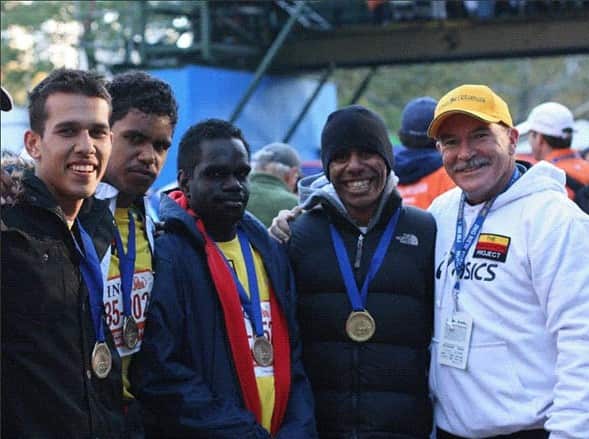 Four First Nations men stand smiling with medals on their neck, after completing the 2010 New York City Marathon. They are joined by Indigenous Marathon Foundation founder, Robert de Castella.