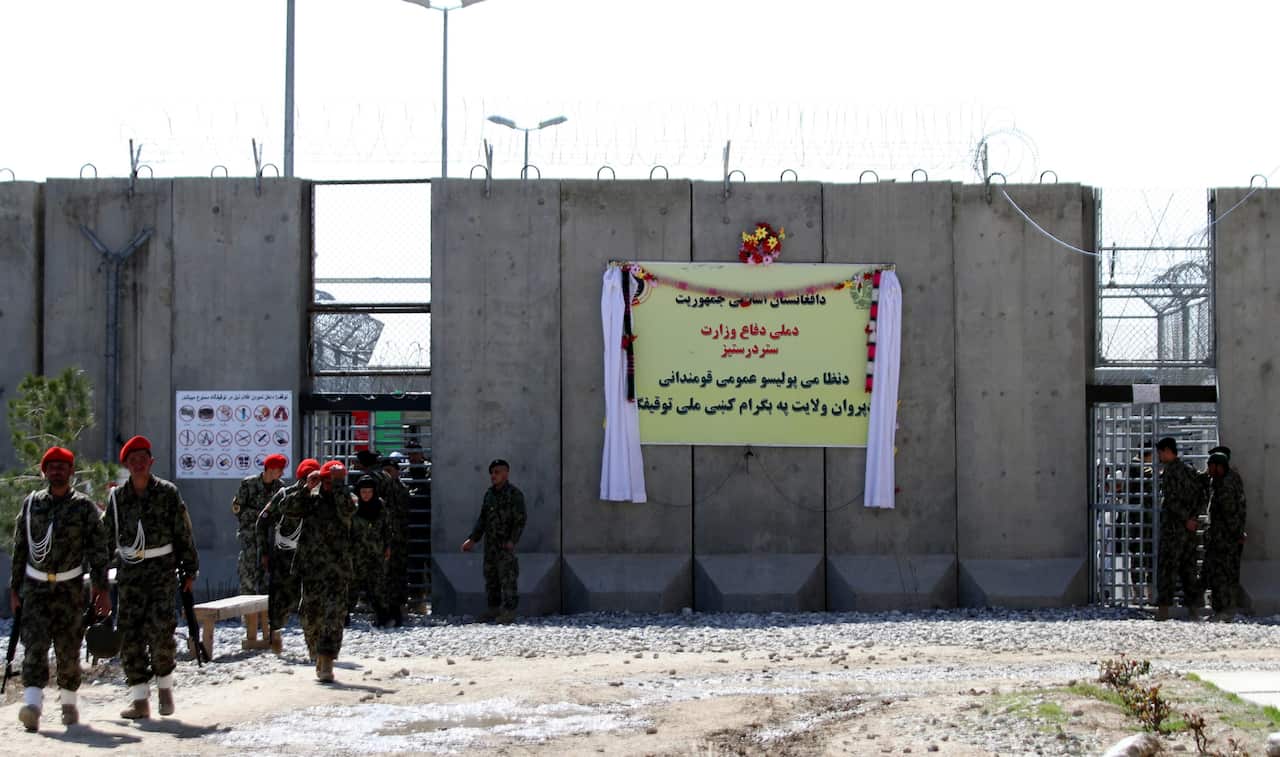 A prison complex in Afghanistan with high concrete walls and a yellow sign written in Dari