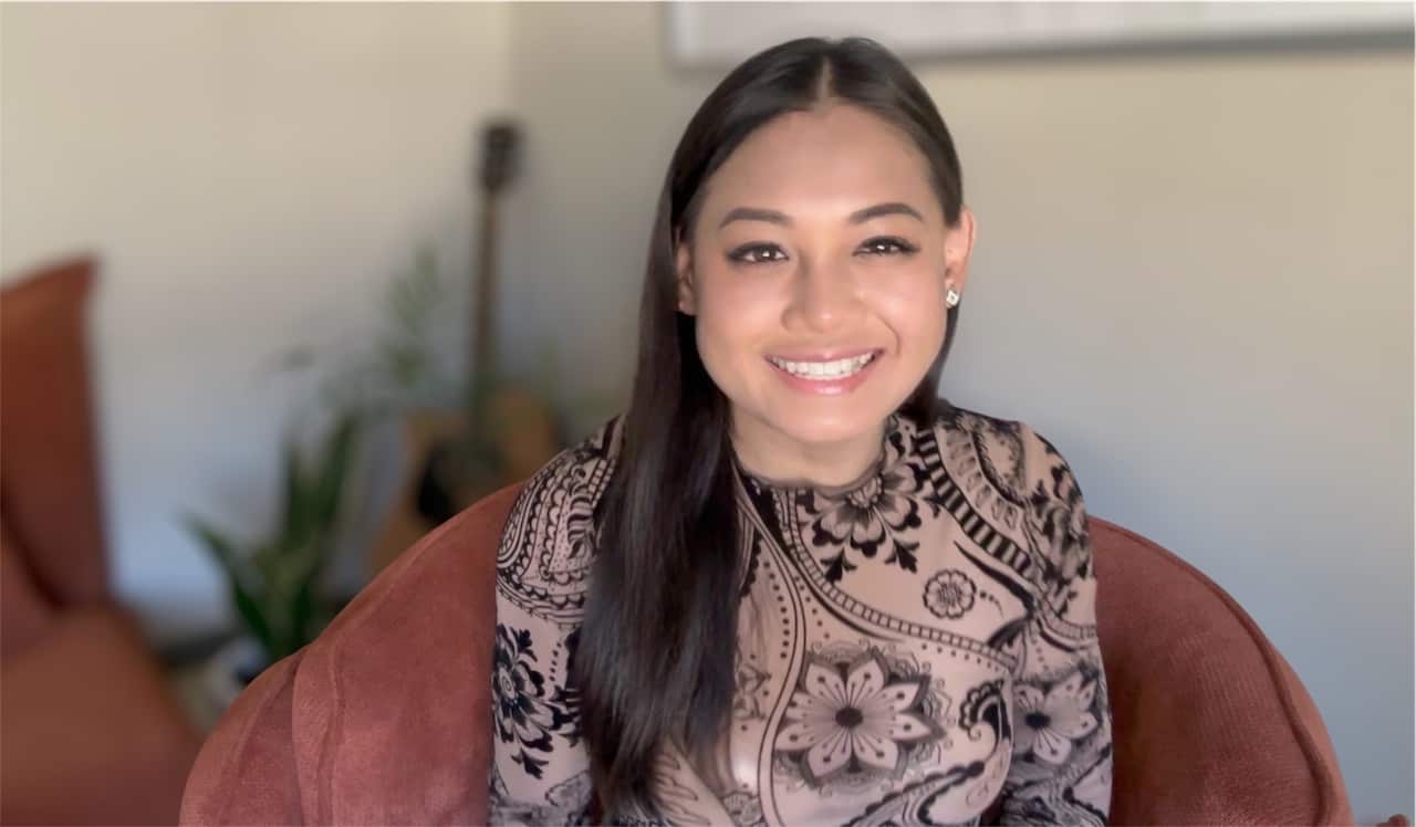 A woman, Jenny, is sitting on a brown coloured chair, looking directly at the camera with a smile