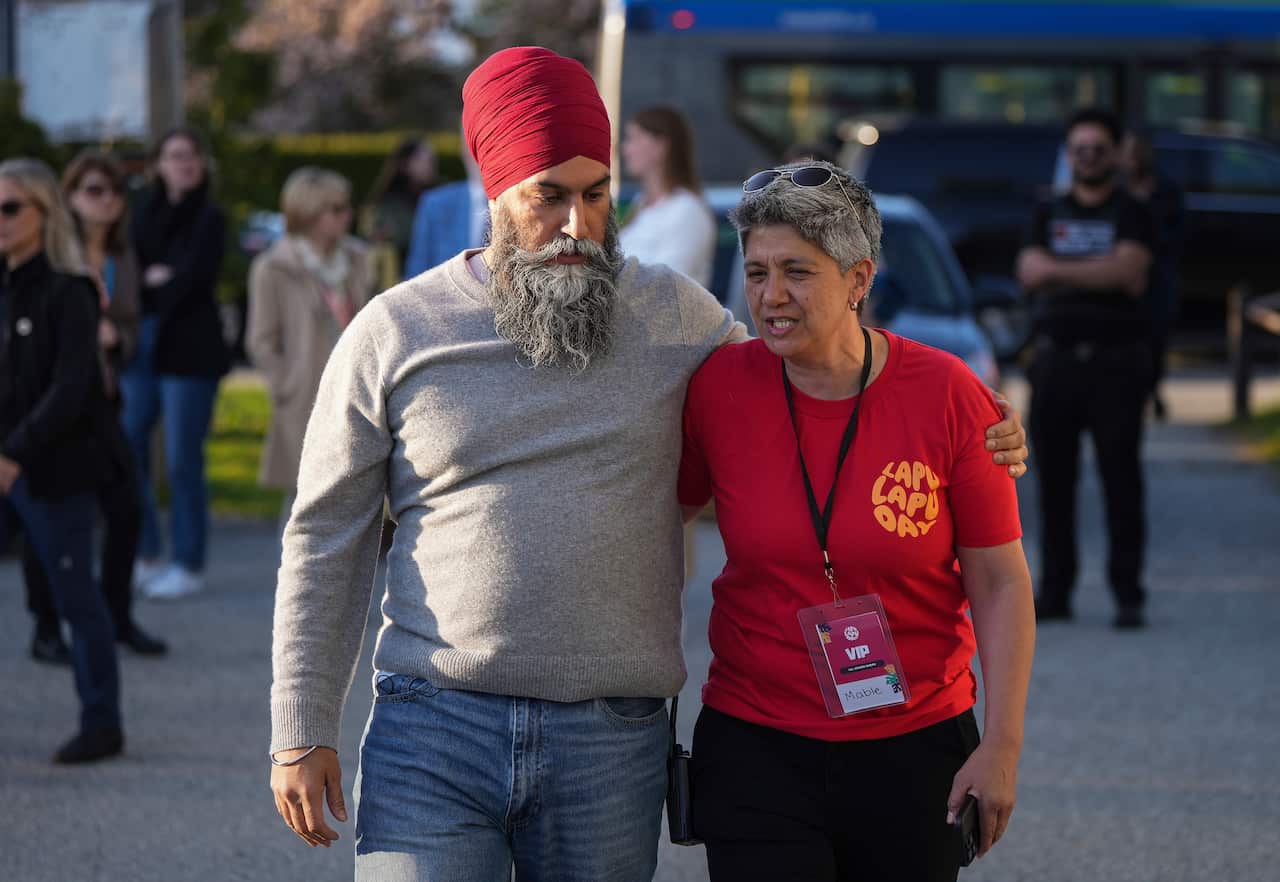 A Sikh man wearing a turban walks down a street with a woman with short grey hair. Their arms are wrapped around each other.