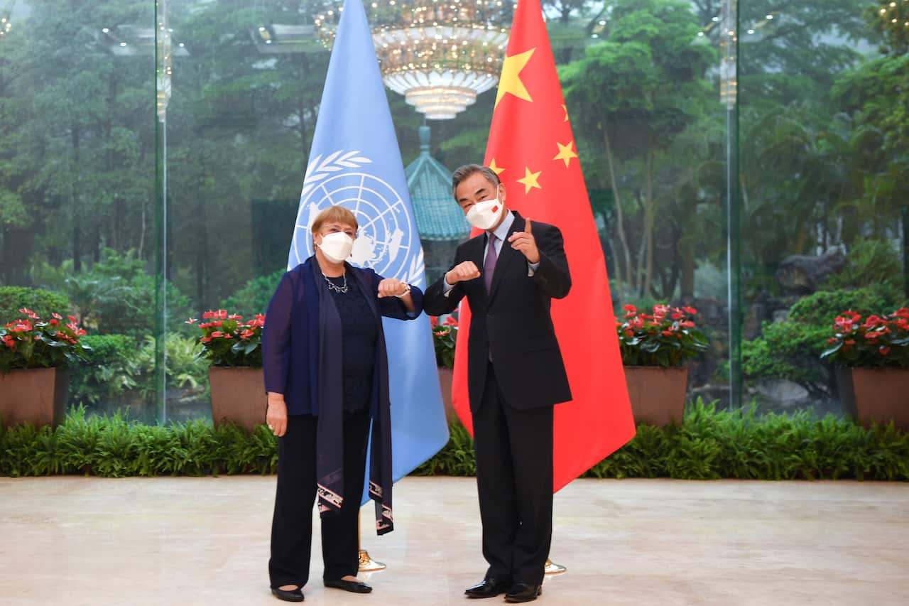 Wang Yi and Michelle Bachelet tap elbows in greeting in front of a UN and CCP flag. 