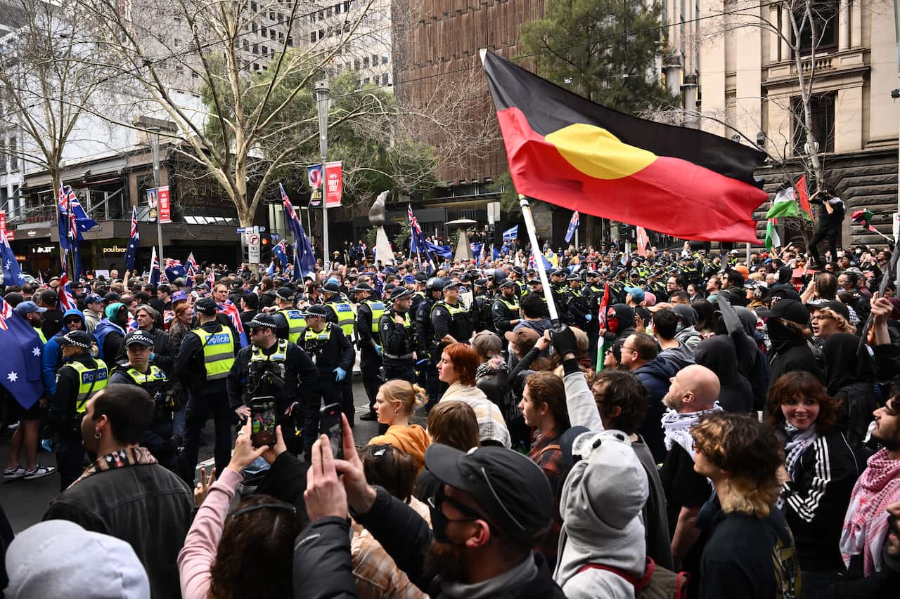 Police separate a crowd of protesters, some of whom are carrying flags and holding their phones.