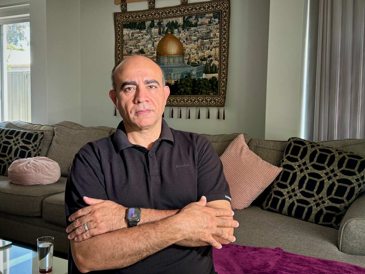 A man with his arms folded poses for a photo while standing in his living room.