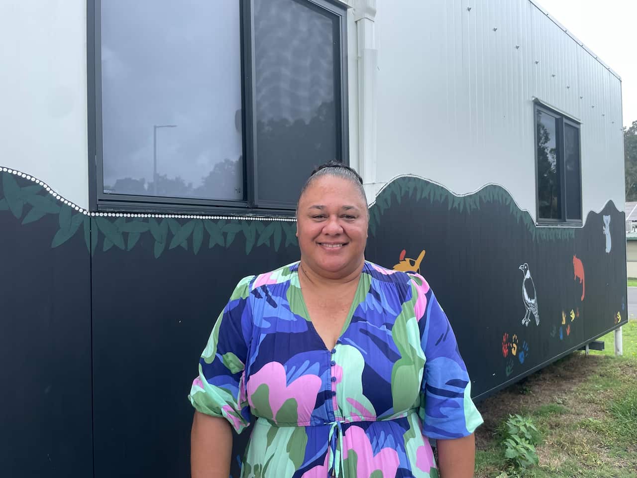A woman in a colourful dress stands in front of a shipping container office. 