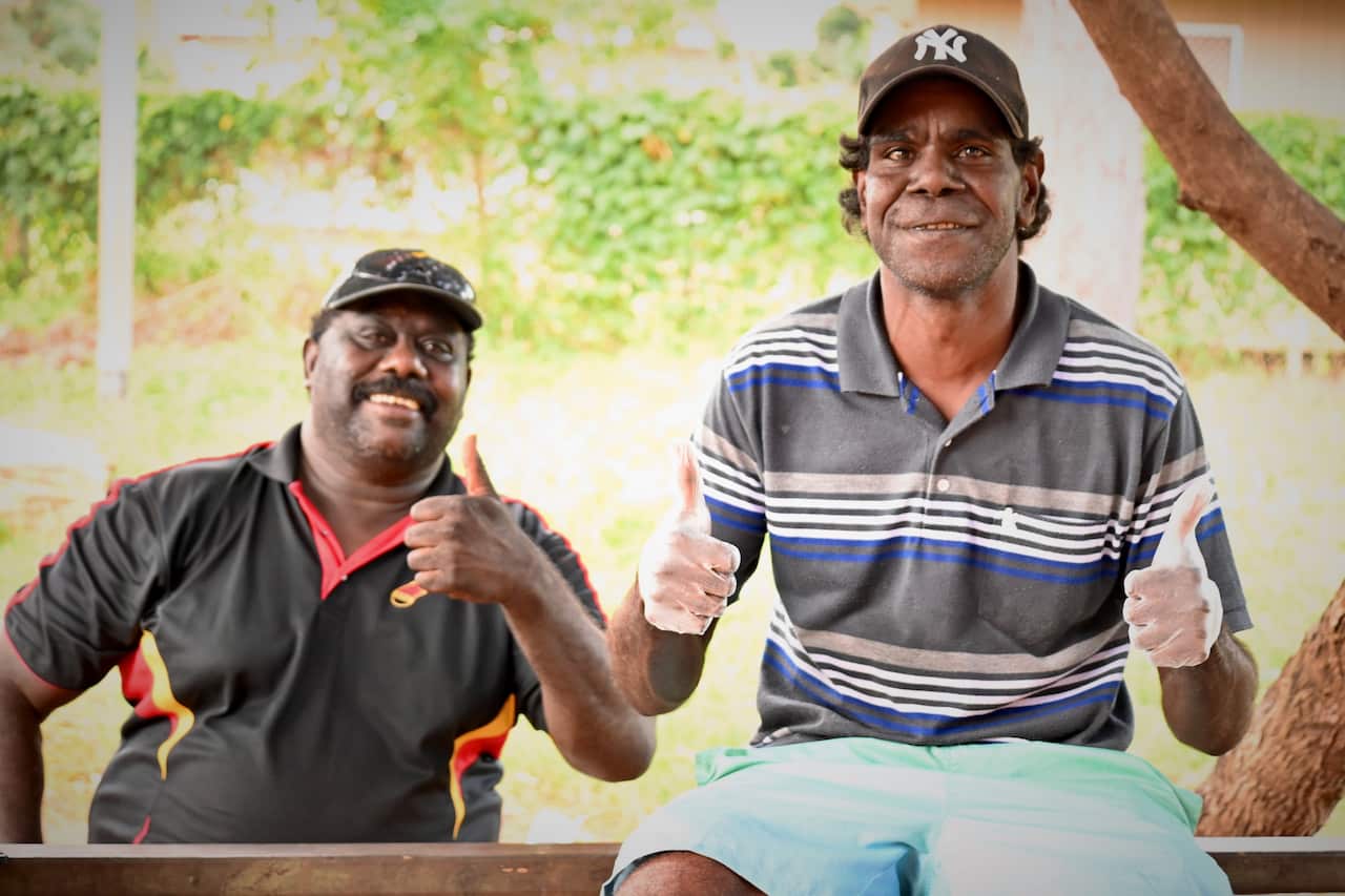 East Arnhem Shire Counsellor Jason Mirrijawuy sits at a picnic table outside the community store with Ramingining resident Marcus Gathiya who has been cleaning up the shopfront