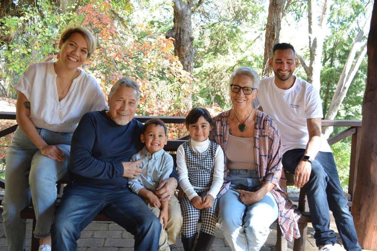Kelly with her father and members of her family seated on a verandah in front of trees. 