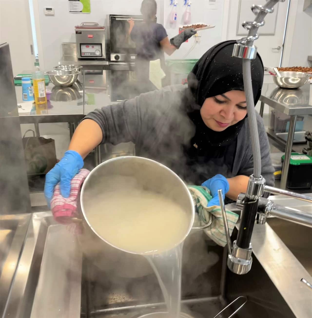 A woman in a grey shirt pours water from a large pot of rice into a sink.