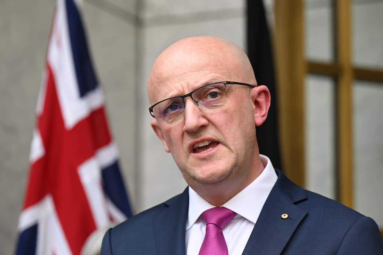 A man in a suit in front of the Australian flag
