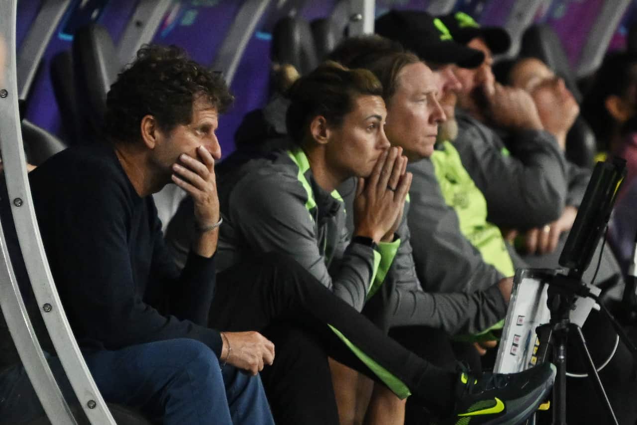 Matildas' players and staff sit nervously with hands over their mouths as they watch the match off to the right of the image