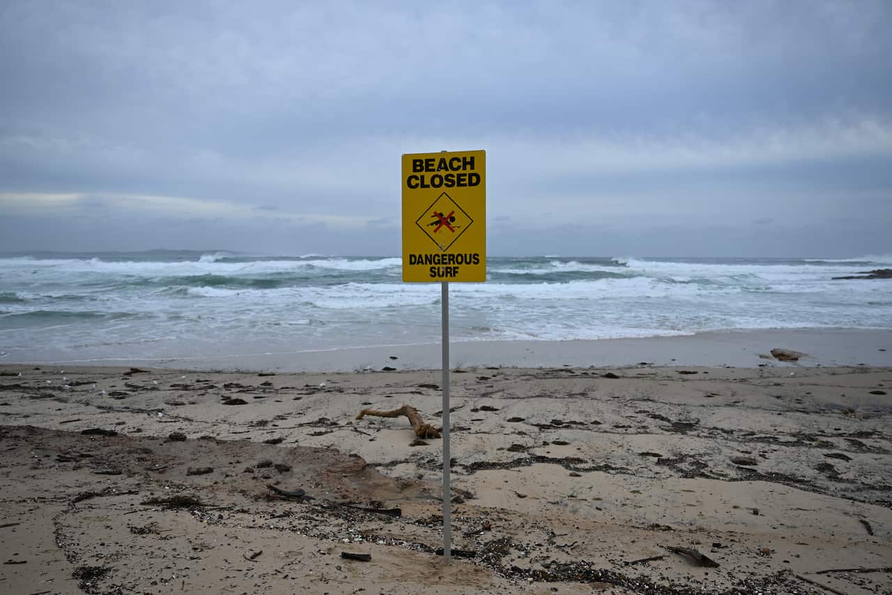 A stormy-looking beach with a sign in the sand that says, 'Beach closed, dangrous surf'.
