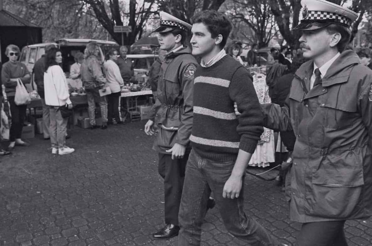 Two police officers walking a man away as people look on. 