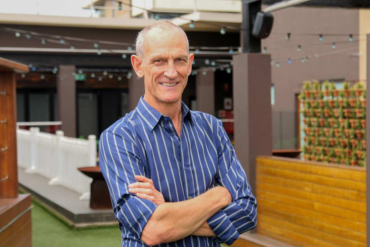 A man in a striped blue shirt stands with his arms crossed, looking down the camers