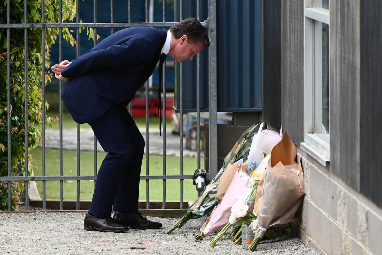 Victorian Deputy Premier Ben Carroll observes a floral tribute outside a school. 