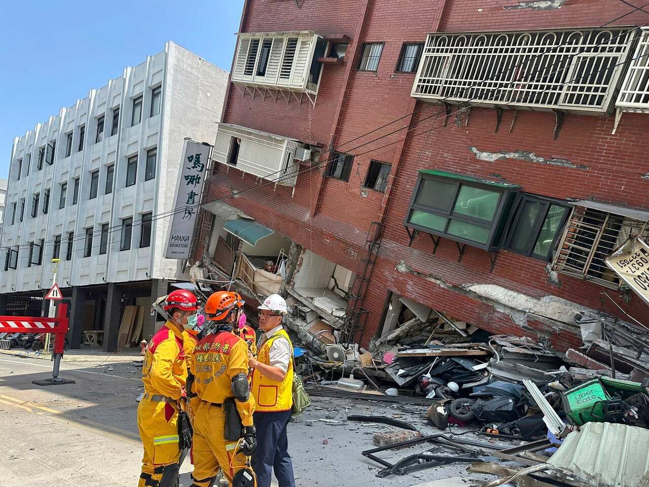 Several people in yellow uniforms stand in front of a collapsed building