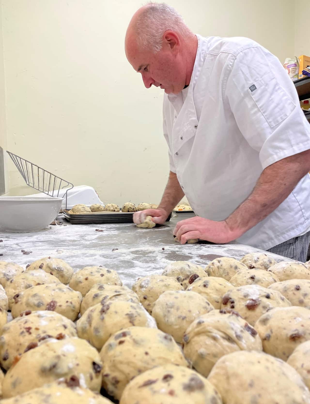 A man in a chef's uniform standing at a counter rolling bread dough.